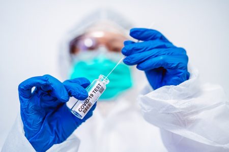 enfermeira usa luvas azuis máscara e roupa de proteção para manusear um teste de covid