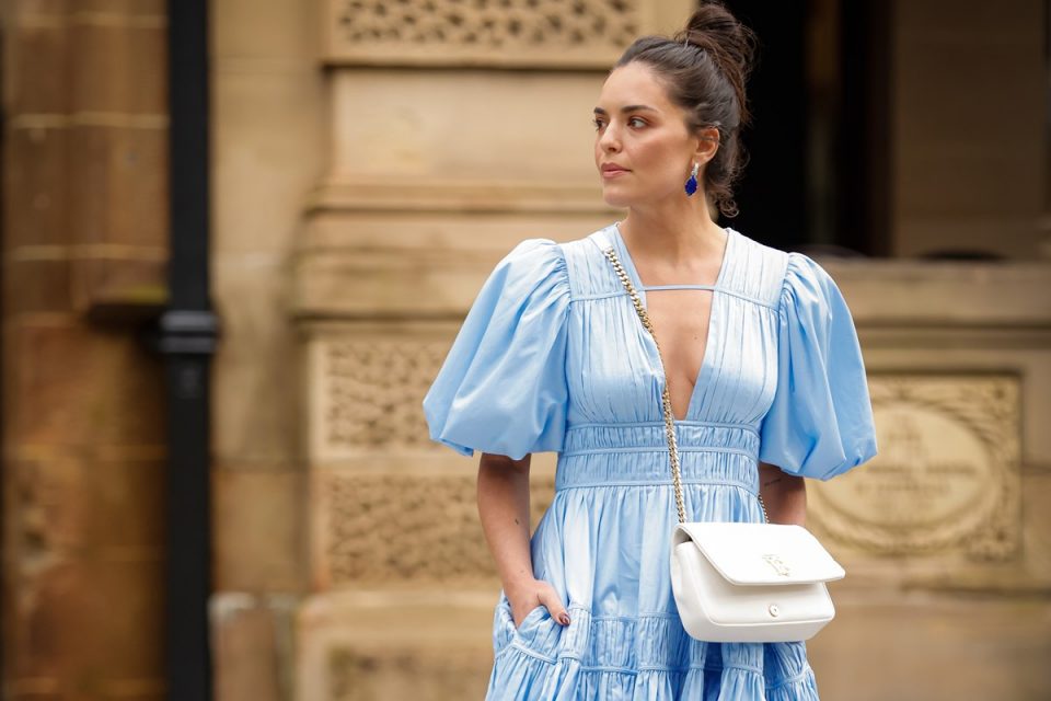 Mulher no street style usando vestido azul claro com franzidos e bolsa branca lateral