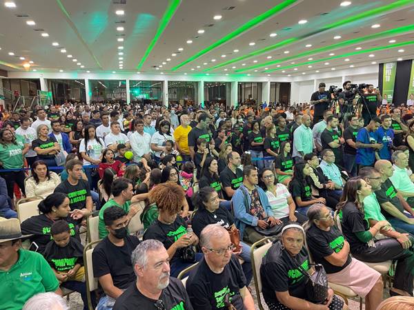 Fotografia colorida de plateia com pessoas vestidas de camiseta preta com escrita verde