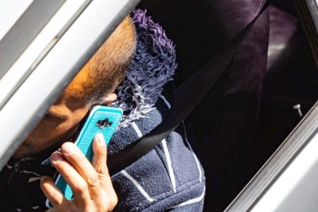 Homem fala ao celular, com capinha azul, enquanto dirige.