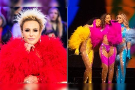 Mulher com cabelo loiro em pé e roupa vermelha com plumas em canto esquerdo da imagem. No canto direito, três mulheres usam roupa amarela, rosa e azul com plumas e se abraçam em palco