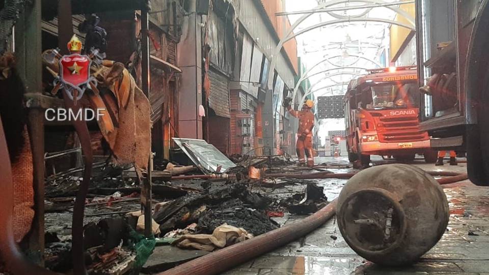 foto colorida de botijão de gás chamuscado com veículos vermelho ao fundo em um corredor