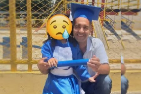 Homem agachado ao lado de menina. Veste capelo, camisa azul clara e calça jeans. Também segura diploma