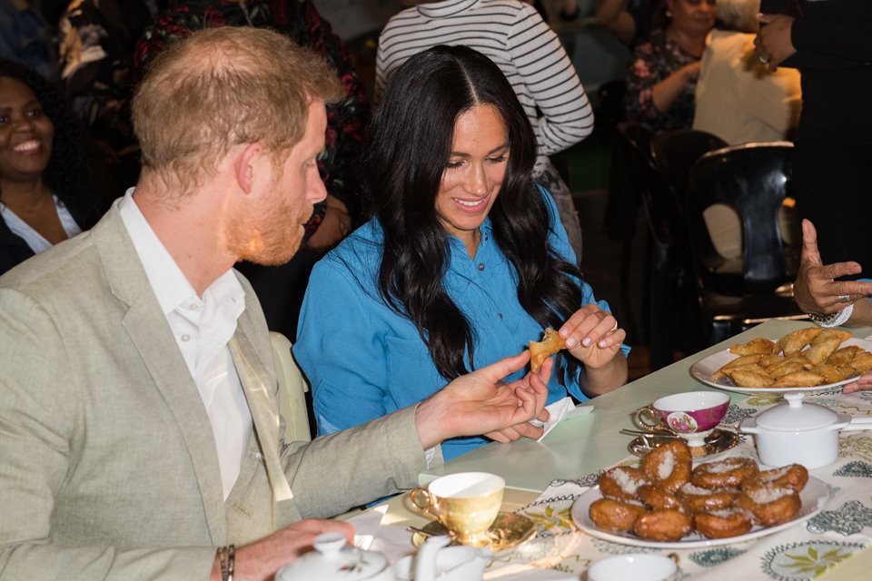 Foto colorida. Príncipe Harry e Meghan Markle comendo