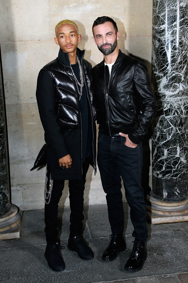 Jaden Smith e o estilista Nicolas Ghesquière em desfile da Louis Vuitton, na Semana de Moda de Paris. Jaden é um jovem rapaz negro, com cabelo raspado descolorido, e Nicolas é branco e mais velho, com o cabelo curto preto. Ambos usam roupas pretas.