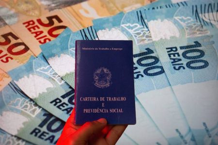 Imagem colorida mostra casteira de trabalho em frente a notas de real - Metrópoles