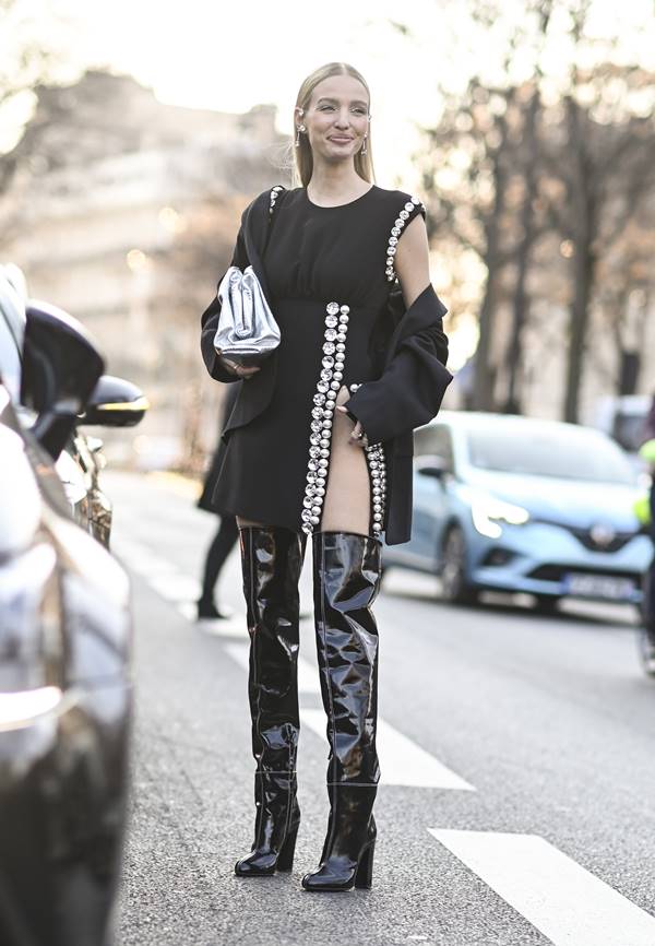 No street style, mulher usa vestido preto com fenda e pérolas, além de bota over the knee
