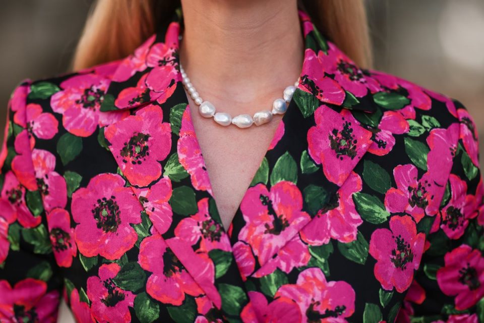 Colar de pérolas em pescoço de mulher loira usando roupa florida