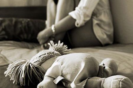 foto em preto e branco de boneca e criança ao fundo sentada em uma cama - Metrópoles