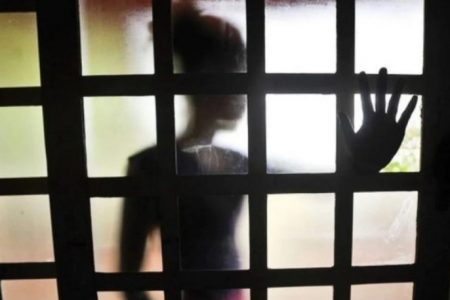 Criança em pé atrás de uma janela quadriculada- Metrópoles