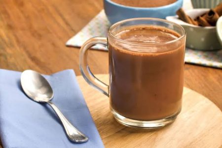 Doce de leite quente em caneca de vidro ao lado de colher. Ambos estão sob tábua de madeira - Metrópoles