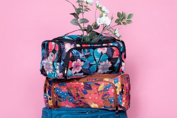 Três bolsas necessaires, estampadas, uma em cima da outra. O fundo da foto é rosa.