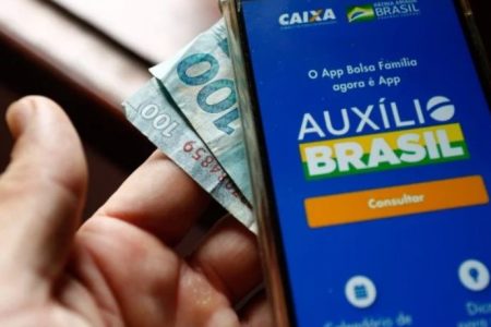 Pessoa segurando celular com dinheiro em baixo -Metrópoles
