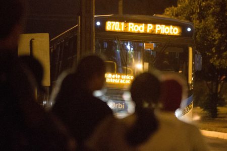 Pessoas vistas de costas esperam ônibus na parada. Em frente, a linha 870.1 que liga a Rodoviária do Plano Piloto ao Riacho Fundo II - Metrópoles