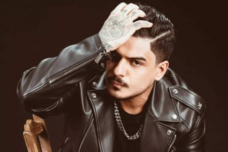 Imagem colorida do DJ Vintage Culture. Ele tem pele clara, cabelo preto, bigode preto, usa uma jaqueta de couro preta, uma camisa preta e um cordão prateado - Metrópoles