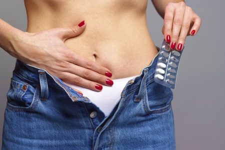 Mulher sem camisa com uma das mãos na barriga enquanto a outra segura remédios- Metrópoles