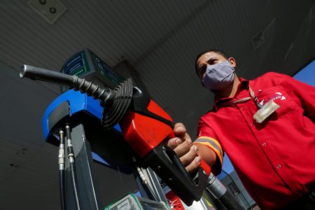 homem com magueira de bomba de gasolina na mão. a mangueira é preta com vermelho