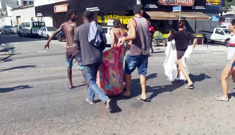 corpo sendo carregado por quatro homens em operação Complexo do Alemão