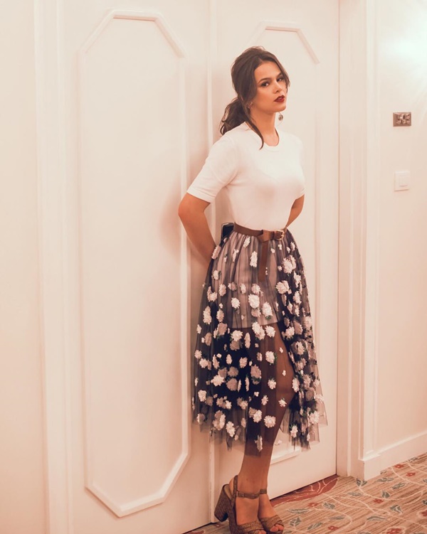 A atriz Bruna Marquezine posando para foto em uma porta de hotel em 2015. Ela usa uma blusa branca e justa e uma saia de tule preta com bolas brancas.