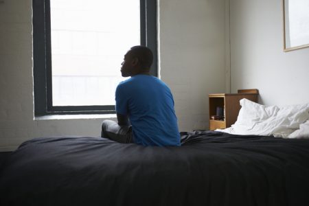 Pessoa sentada em cama olhando para a janela - Metrópoles