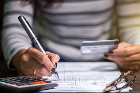 Imagem colorida mostra pessoa fazendo contas com uma calculadora e segurando cartão - Metrópoles