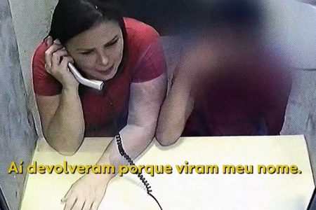 Mulher com camisa vermelha e mão em mesa falando ao telefone