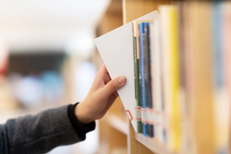 Imagem de uma pessoa pegando um livro na estante de uma biblioteca