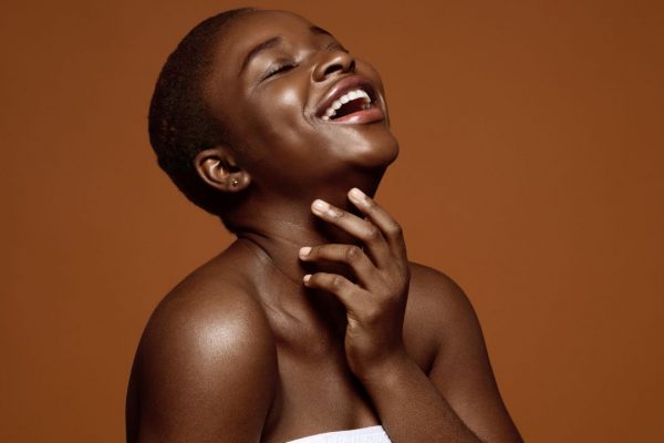 Mulher com uma mão no pescoço, sorrindo para cima de olhos fechados - Metrópoles