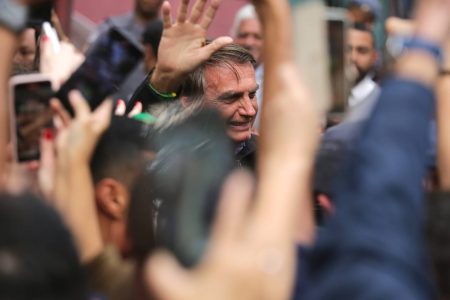 Candidato à reeleição, Jair Bolsonaro (PL) cumprimenta apoiadores na saído do Bar da Dirce, em São Paulo. Ele acena para as pessoas no meio de uma multidão, usando jaqueta preta - Metrópoles