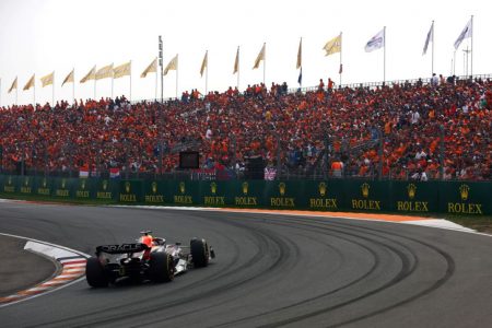 imagem colorida de pista de corria e carro em fazendo curva para a esquerda e arquibancada lotada na direita - Metrópoles