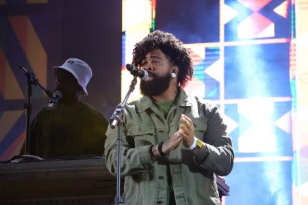 Homem negro cantando no palco. Ele tem cabelo crespo e preto, barba preta e usa um look verde escuro, com jaqueta - Metrópoles