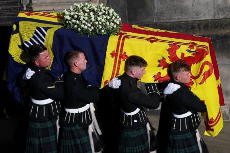 Foto colorida. Homens seguram um caixão com a bandeira da monarquia