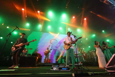 banda tocando em palco com luzes coloridas - metrópoles