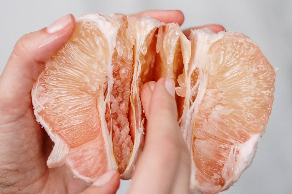 Foto colorida de duas mãos segurando uma toranja e passando os delos no meio da fruta, em close - Metrópoles