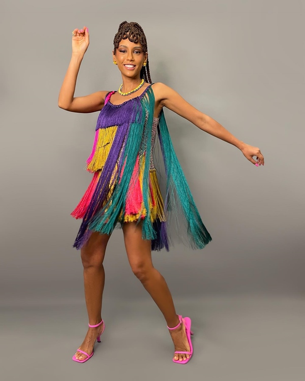 A atriz Tais Araujo posando para foto em um fundo cinza. Ela usa um vestido colorido de cordas