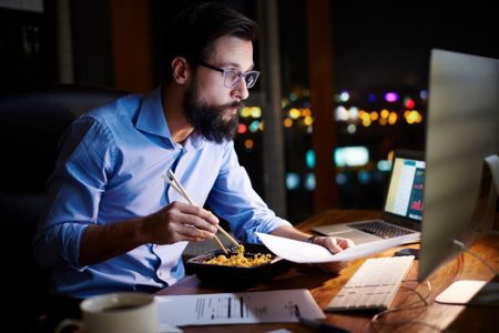 Homem come em frente ao computador