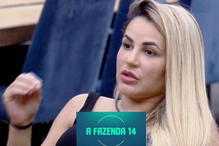 Na foto, Deolane Bezerra está gesticulando com a mão direita, usando regata, tem cabelo loiro e o logo de A Fazenda 14 está estampado no centro inferior da imagem - Metrópoles