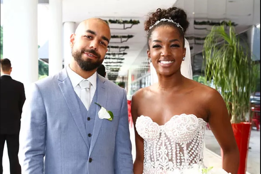 Foto colorida de IZA e Sérgio Santos durante casamento. Cantora está vestida de noiva e ele, de terno - Metrópoles