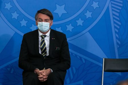 O presidente Jair Bolsonaro de máscara, sentado no salão de eventos do Palácio da Alvorada. Sob fundo azul, ele olha para baixo, usa terno e está de mãos cruzadas - Metrópoles