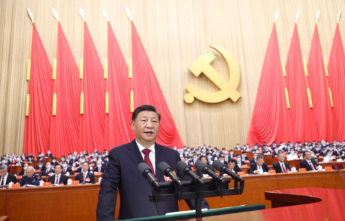 Presidente Xi Jinping da China discursa em sede do Partido Comunista Chinês, de costas para a plateia. Ao fundo, bandeiras vermelhas e o símbolo do comunismo, uma foice com martelo - Metrópoles