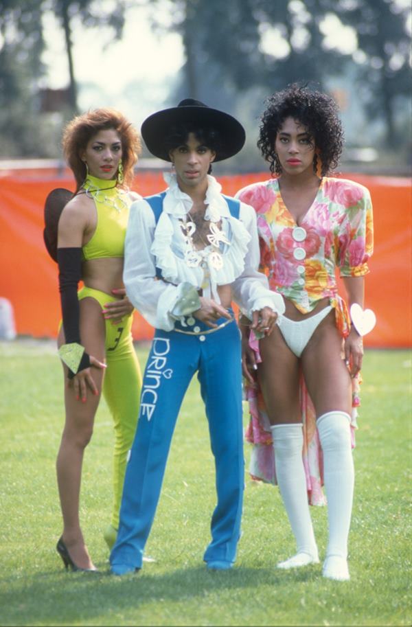 Na imagem com cor, Prince ao lado de duas mulheres