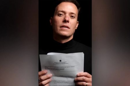 O Pastor André Valadão está vestido de preto e mostra um documento em sua mão. Ele é branco, tem cabelo preto e utiliza roupas pretas - Metrópoles