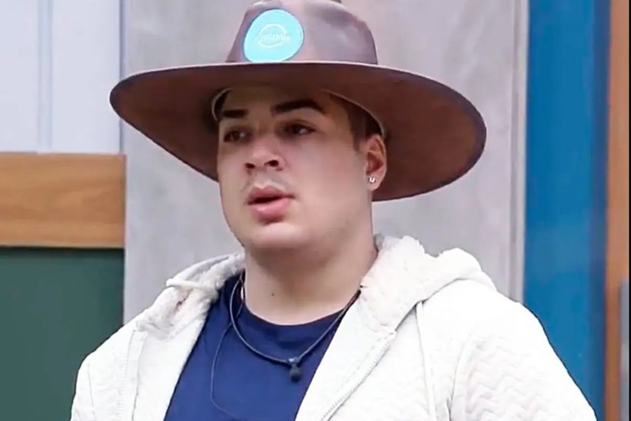 Lucas Santos em A Fazenda 14. O homem está com um chapéu marrom, blusa azul escura, casaco branco e tem pele clara - Metrópoles