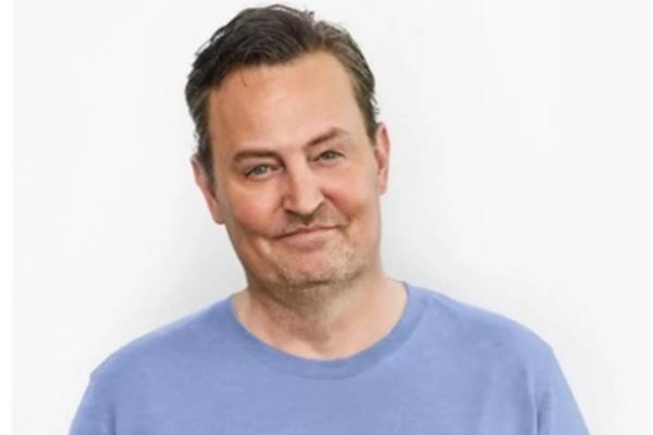 Ator Matthew Perry de camiseta azul em fundo branco - Metrópoles