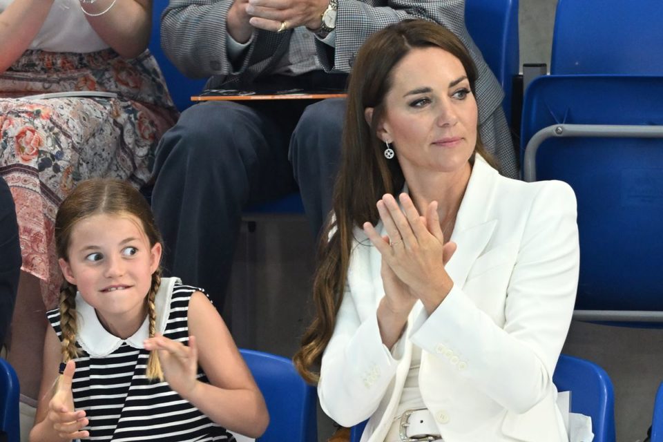 Foto colorida. Menina com os olhos arregalados ao lado de mulher branca com terno branco e batendo palmas- Metrópoles