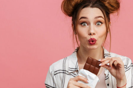 Imagem colorida de mulher comendo chocolate - Metrópoles