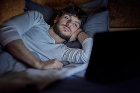 Foto colorida de homem deitado olhandop ara a tela do computador -Metrópoles