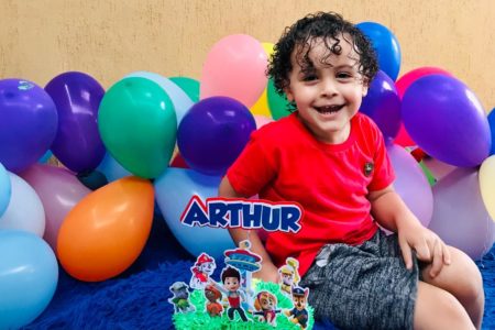 Menino de cabelos cacheados e camiseta vermelha, sorrindo para foto