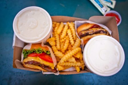 Na foto, dois hamburgueres, batata frita e refrigerante vistos de cima. - Metrópoles