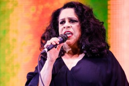 Foto colorida de Gal Costa. ela está cantando com o microfone na mão e utiliza uma roupa preta. Ele também tem o cabelo preto - Metrópoles